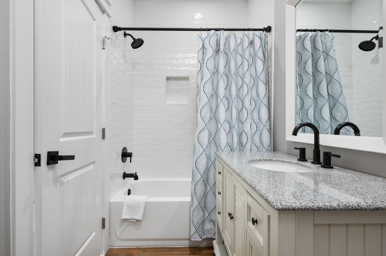 Une salle de bain moderne avec une baignoire, une douche, un lavabo avec un miroir et un rideau de douche à motifs.