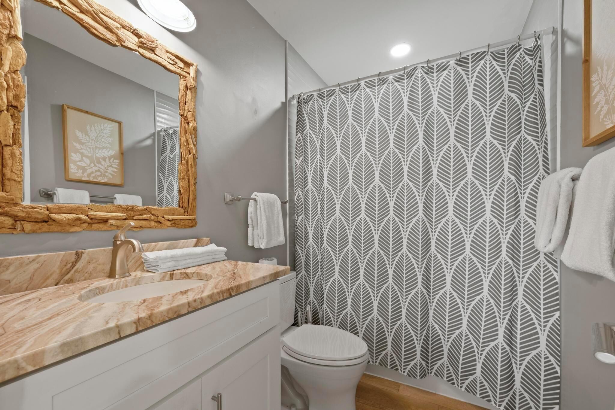 A bathroom with a marble sink, a white toilet, and a shower curtain with a leaf pattern.
