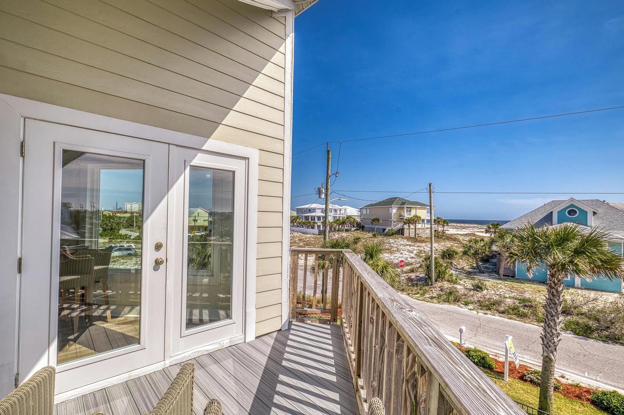 A coastal property with a wooden deck, glass doors, and a view of the beach and ocean.