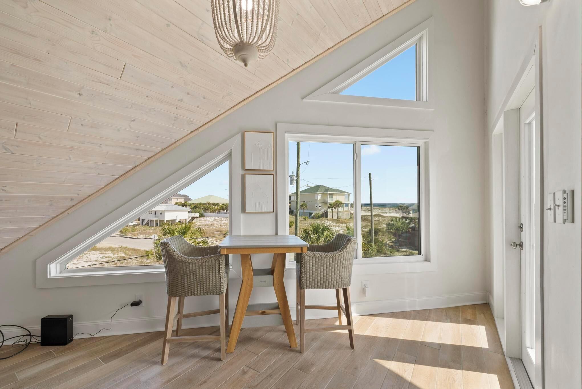 A room with a sloped ceiling, large windows, a table, two chairs, and a chandelier.