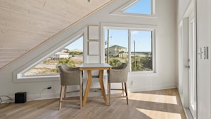 Une pièce avec un plafond en pente, de grandes fenêtres, une table, deux chaises et un lustre.