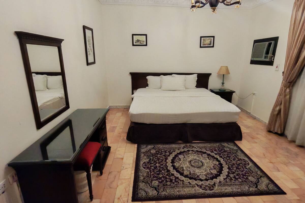 A bedroom with a bed, a desk, a chair, a rug, and a mirror.