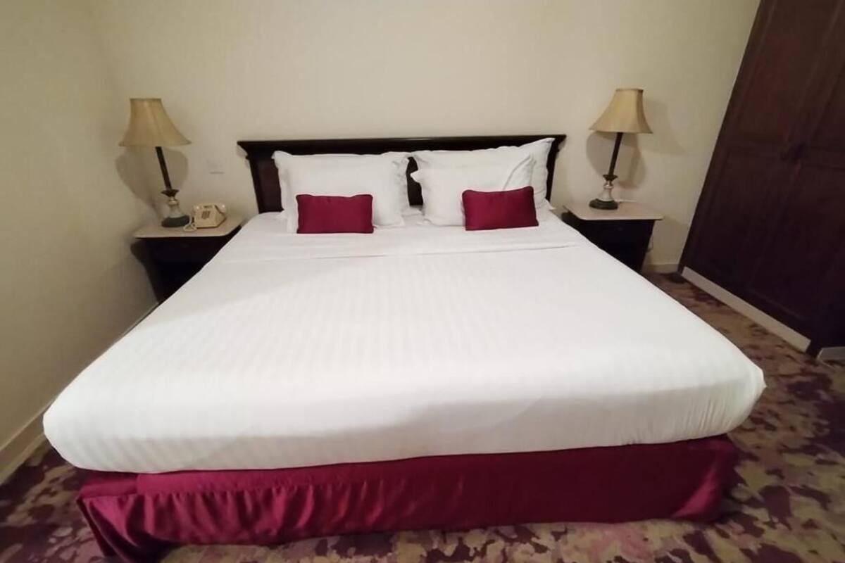A neatly made bed with white and red bedding, two bedside lamps, and a patterned carpet.