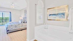 A bedroom with a bed, a large window, a ceiling fan, and a bathroom with a bathtub and a framed picture. - Upstay Family-Friendly Condo w Pool Near Disney (Winter Garden)
