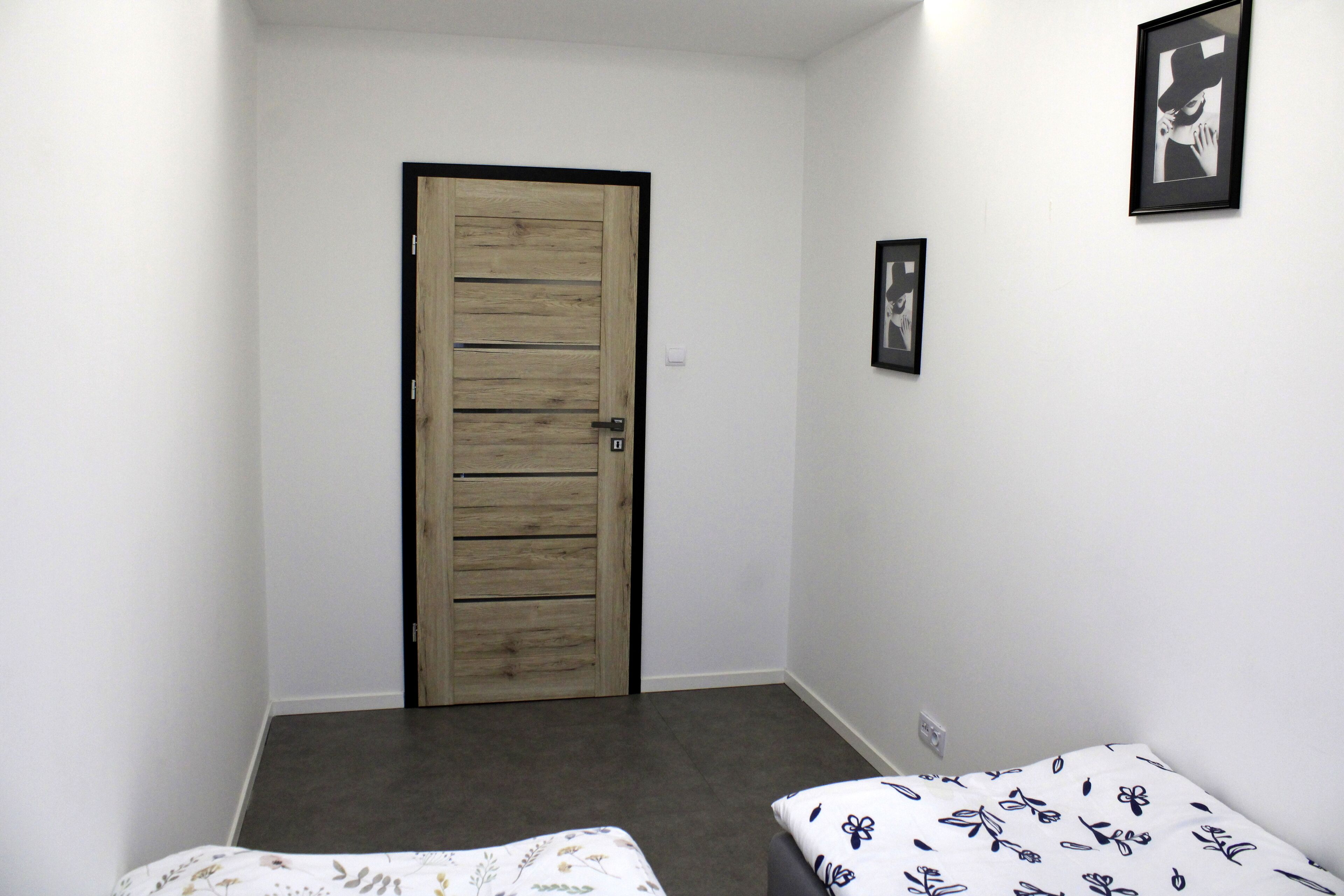 A bedroom with a wooden door, a bed with a floral bedspread, and two framed pictures on the wall.