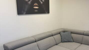 Un canapé d’angle gris avec un coussin, une œuvre d’art encadrée accrochée au mur et un spot encastré au plafond.