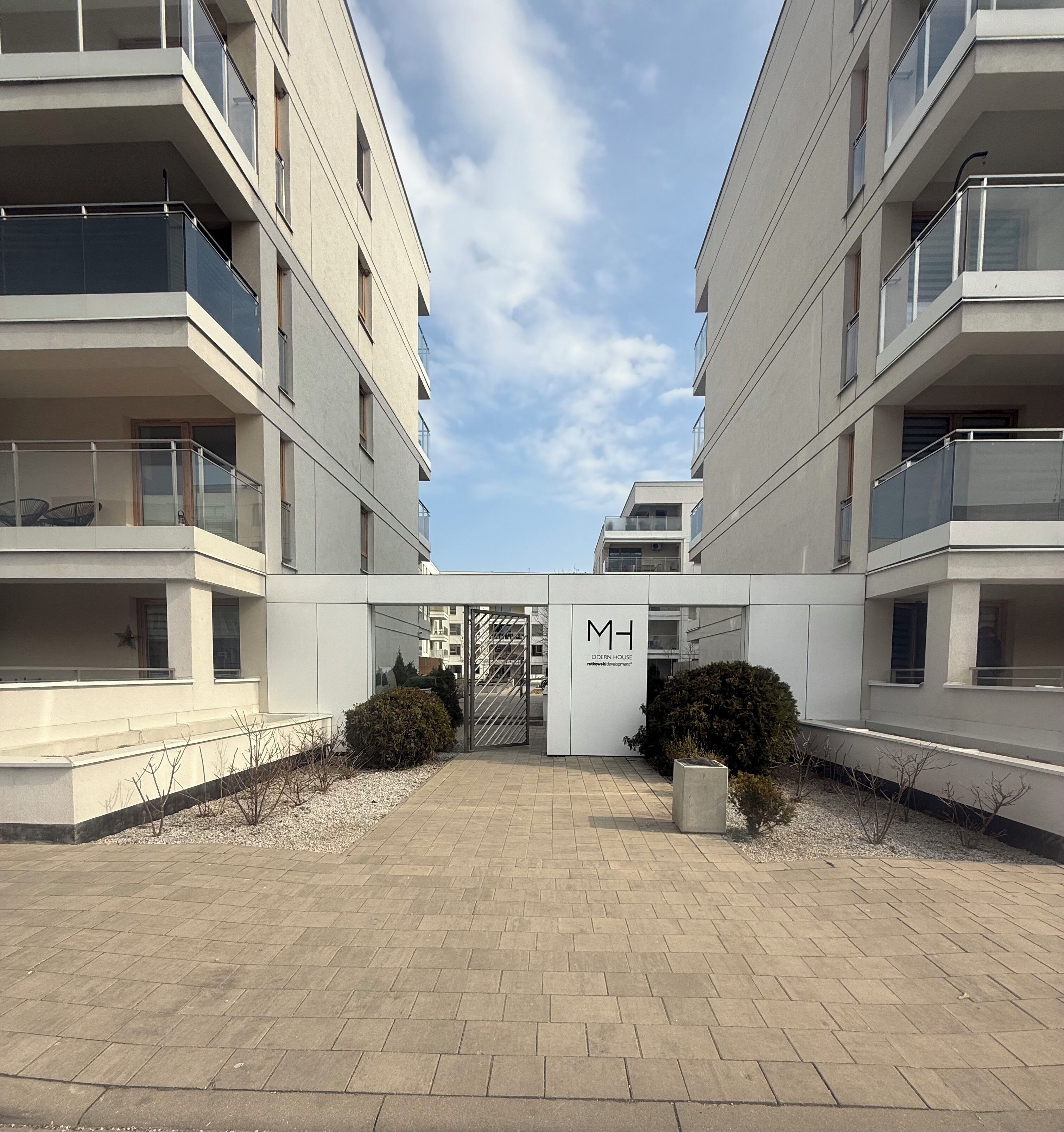 Een modern appartementencomplex met een centrale ingang, balkons en een heldere lucht.