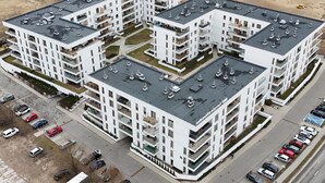 Moderni, useita kerroksia korkea asuinkerrostalo, jossa on parvekkeita, pysäköintialue ja taustalla rakennustyömaa.