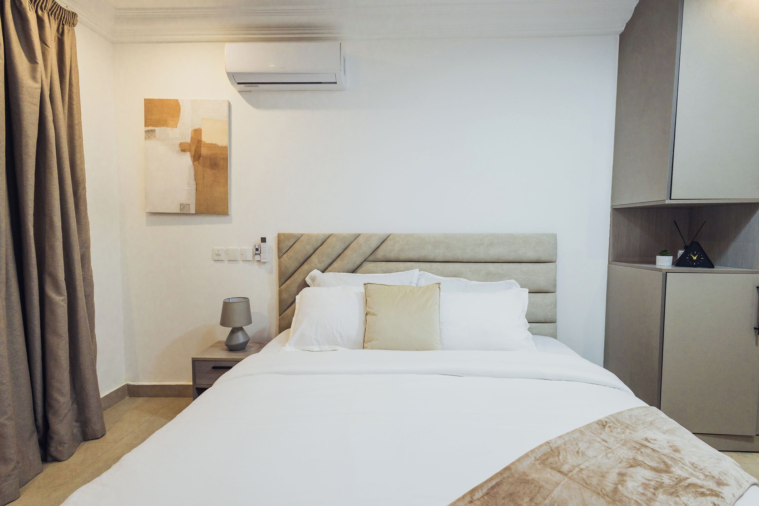 Ein Hotelzimmer mit Bett, Nachttisch, Lampe, Klimaanlage, Schrank und einem Bild an der Wand.