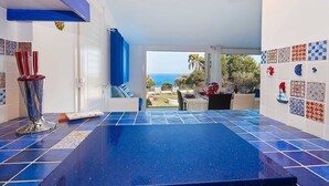 A kitchen with a view of the sea, a dining area with a table and chairs, and a blue-tiled floor.