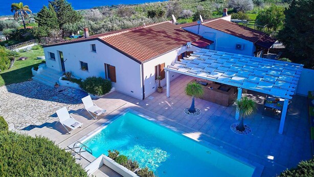 A villa with a swimming pool, a covered patio, and a view of the sea.