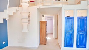 A modern interior with a staircase, a wooden cabinet, and a hallway leading to a door with blue panels.