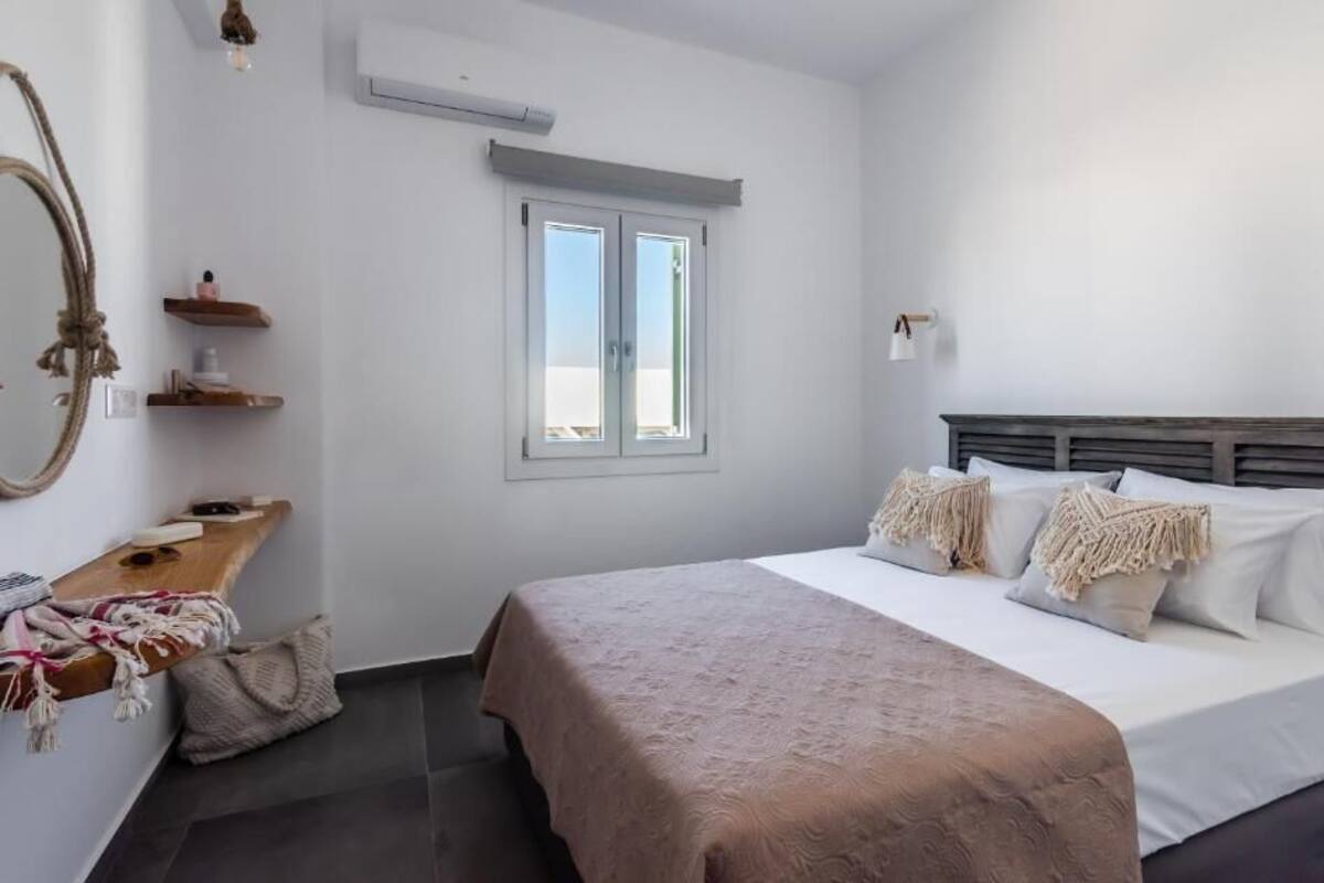 A bedroom with a bed, a bedside table, a mirror, a window, and a wall-mounted air conditioner.