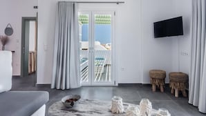 Ein modernes Wohnzimmer mit einer Couch, einem Couchtisch mit Gläsern, einem Fernseher und einem Balkon mit Blick.