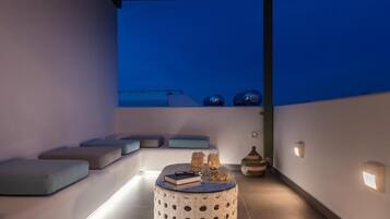 A modern outdoor seating area with a round table, cushions, and decorative items.