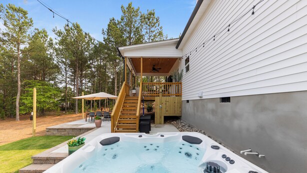 A hot tub in a backyard with a wooden deck and stairs leading to a balcony. - 6BR w/ Golf Sim Putting Green Hot Tub Sauna Games (Pinehurst)