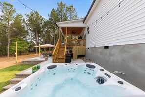 Un jacuzzi en un patio trasero con terraza de madera y escaleras que llevan a un balcón.
