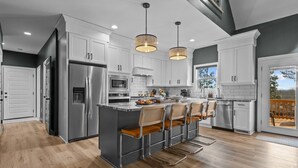 A modern kitchen with stainless steel appliances, a central island with bar stools, and pendant lighting. - 6BR w/ Golf Sim Putting Green Hot Tub Sauna Games (Pinehurst)
