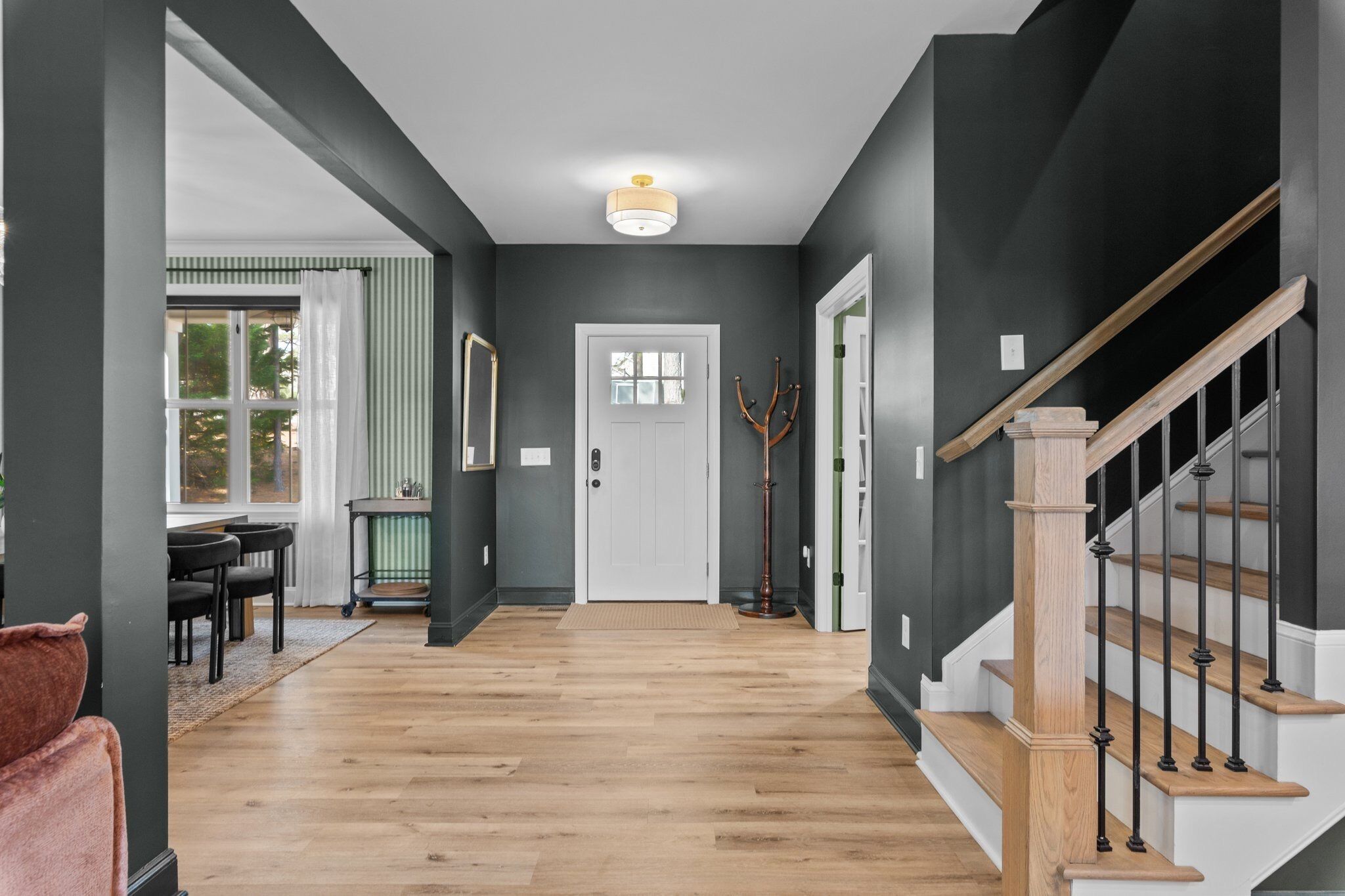 A hallway with a wooden floor, a staircase with a wooden handrail, and a white door at the end.