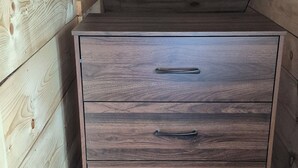 Un meuble en bois doté de quatre tiroirs et d’une poignée en métal, situé dans un coin dont les murs sont en bois et le plafond est en pente.