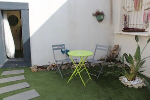 A small outdoor seating area with a table and two chairs, surrounded by rocks and plants.