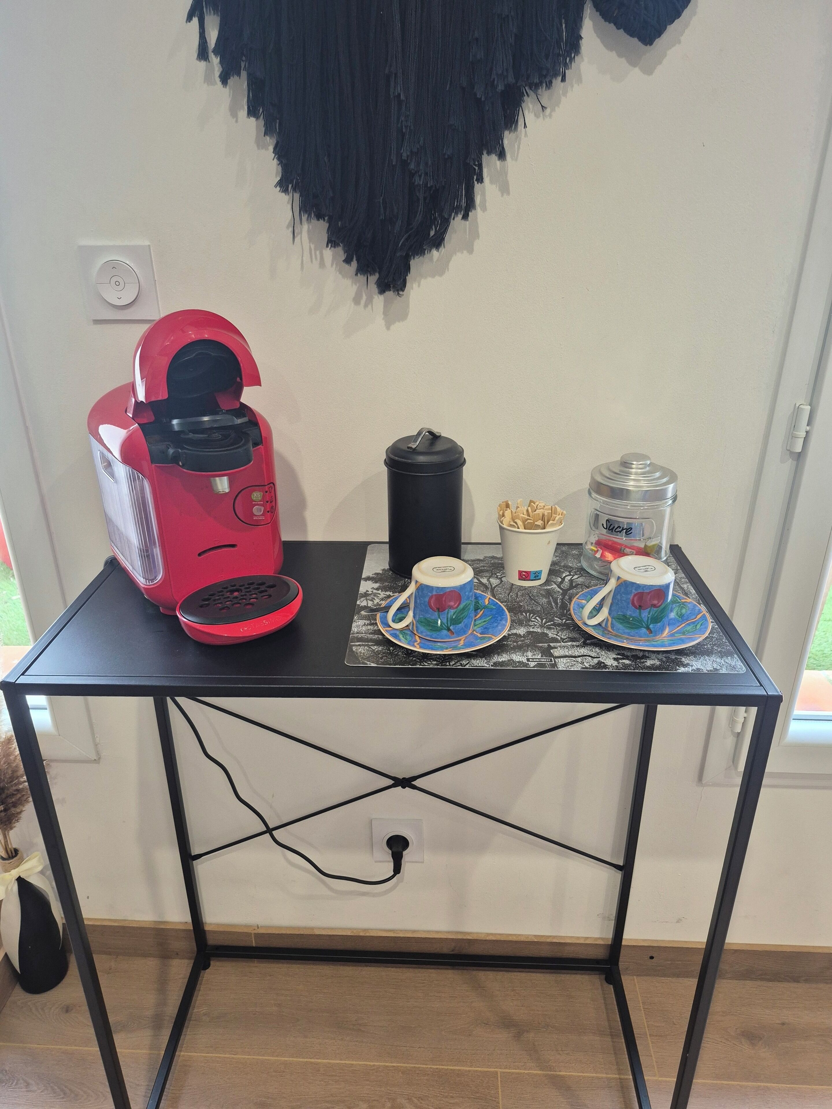 A small table with a red coffee maker, a black thermos, and two cups with saucers.