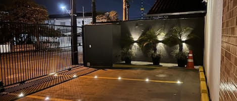 A gated parking area at night with illuminated potted plants and a clear path marked by yellow lines.