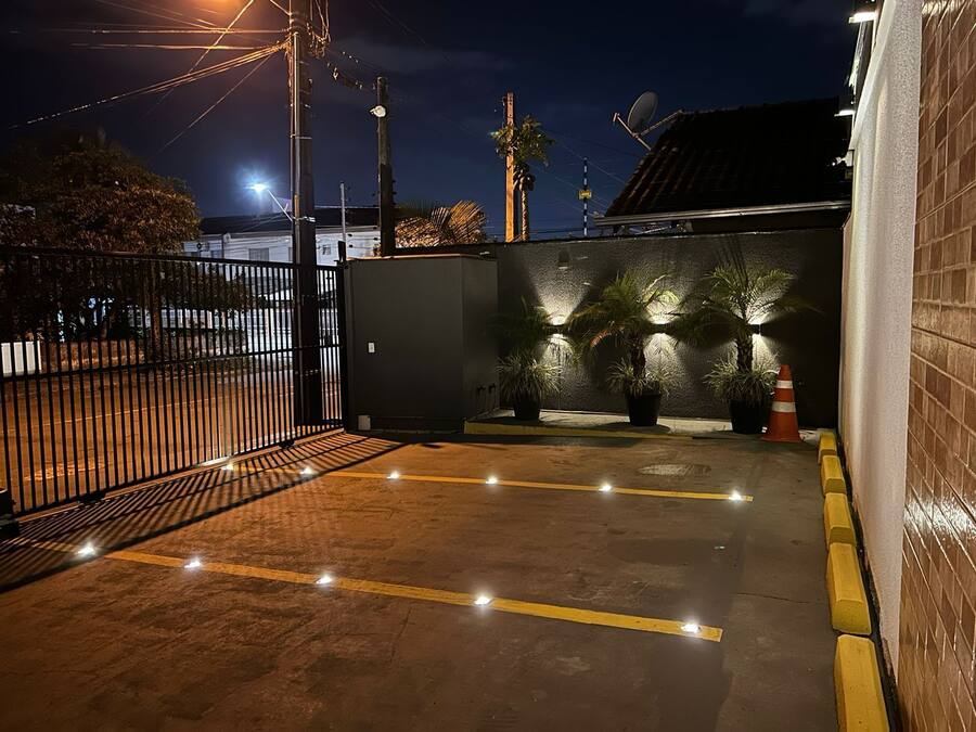 A gated parking area at night with illuminated potted plants and a clear path marked by yellow lines.