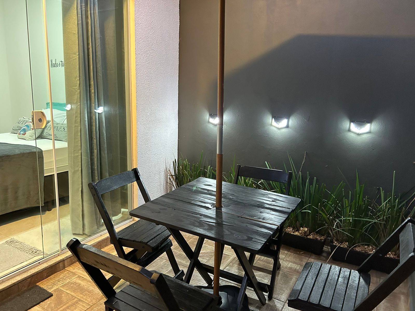 A modern outdoor seating area with a table and chairs, surrounded by potted plants and illuminated wall lights.