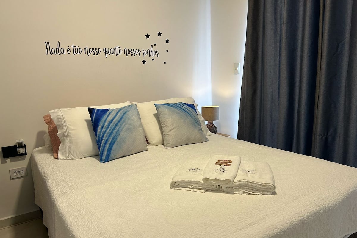 A neatly made bed with a white quilt, three pillows, and a folded towel on the bed.