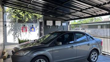 Um carro estacionado sob uma cobertura com portão e um edifício com uma placa ao fundo.