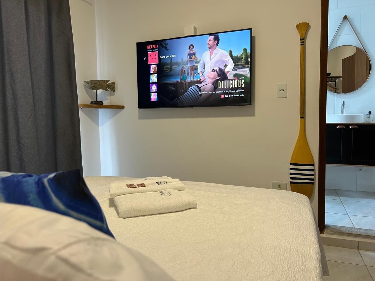 Habitación de hotel con cama, televisor de pantalla plana mostrando una película, remo de madera y espejo redondo en la pared.