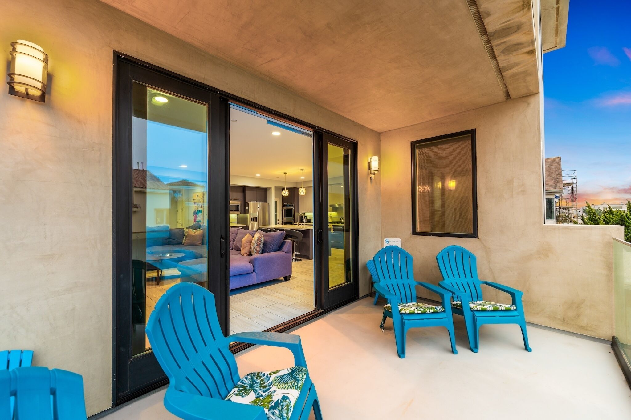 A balcony with blue chairs, a glass door leading to a living area, and a cityscape view.