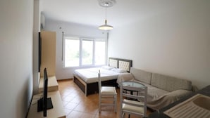 Una habitación pequeña y bien iluminada con una cama, un sofá, una mesa de comedor y un televisor.