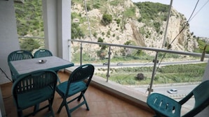 Un balcón con una mesa y sillas, con vistas a una carretera y un paisaje montañoso.