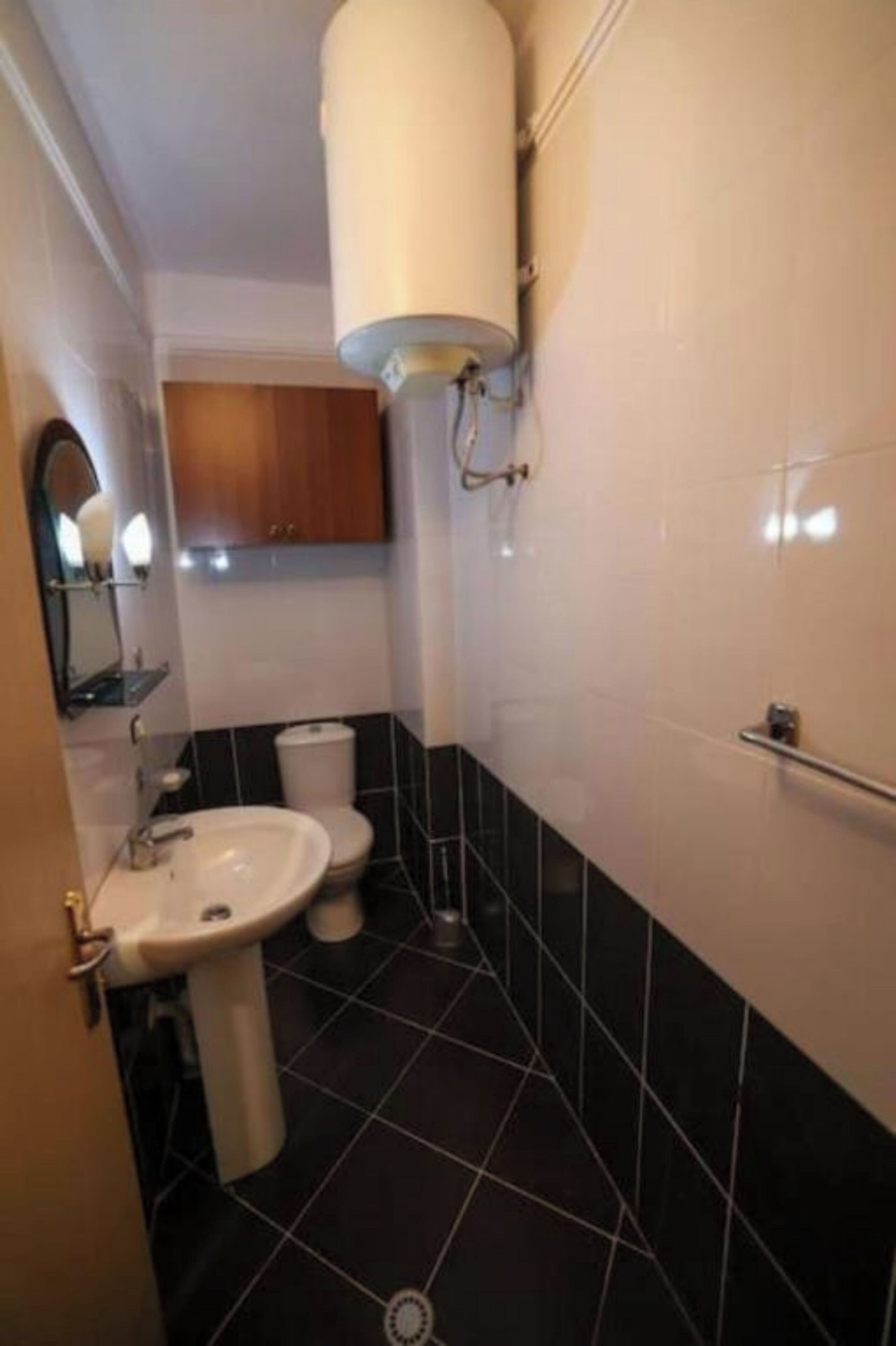 Une salle de bain avec un lavabo blanc, des toilettes et un chauffe-eau cylindrique fixé au mur.