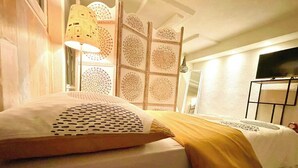 A neatly made bed with patterned pillows, a decorative wall panel, a standing lamp, and a television on a stand. - Guest Room, Enjoy the peaceful Bernese Seeland (Grossaffoltern)