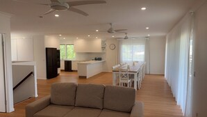 Un salon moderne avec un canapé, un coin repas avec une table et des chaises, une cuisine équipée d’un réfrigérateur et de placards, et un ventilateur de plafond.