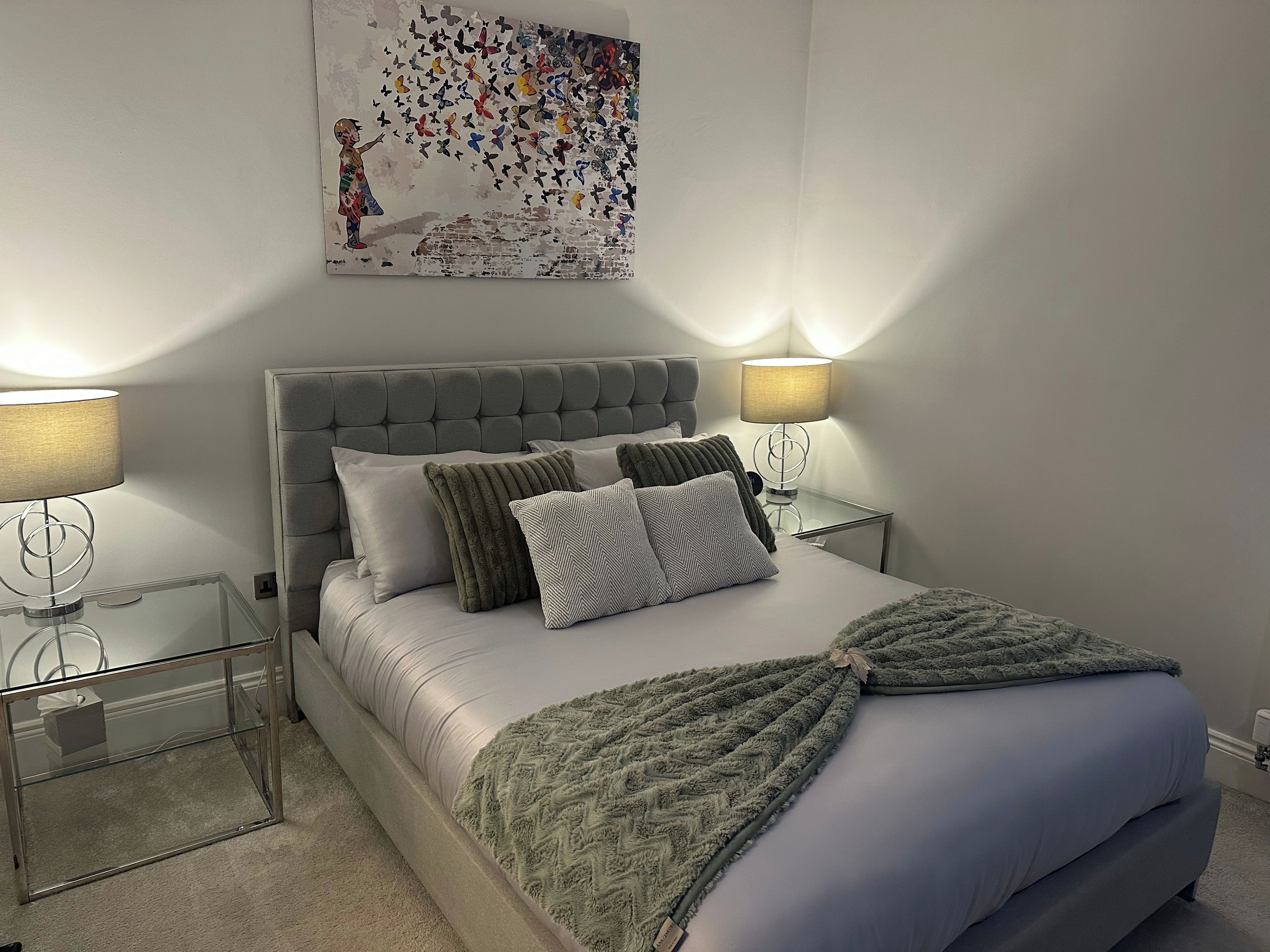 A bedroom with a bed, two bedside tables, a wall-mounted lamp, and a decorative wall piece.
