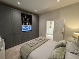 Une chambre avec un grand lit, un téléviseur encastré, des armoires grises et une porte donnant sur une autre pièce.