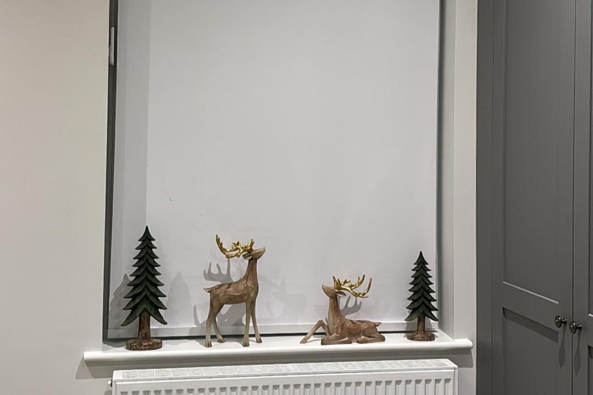 A fireplace mantel with three deer figurines and two small pine tree decorations.