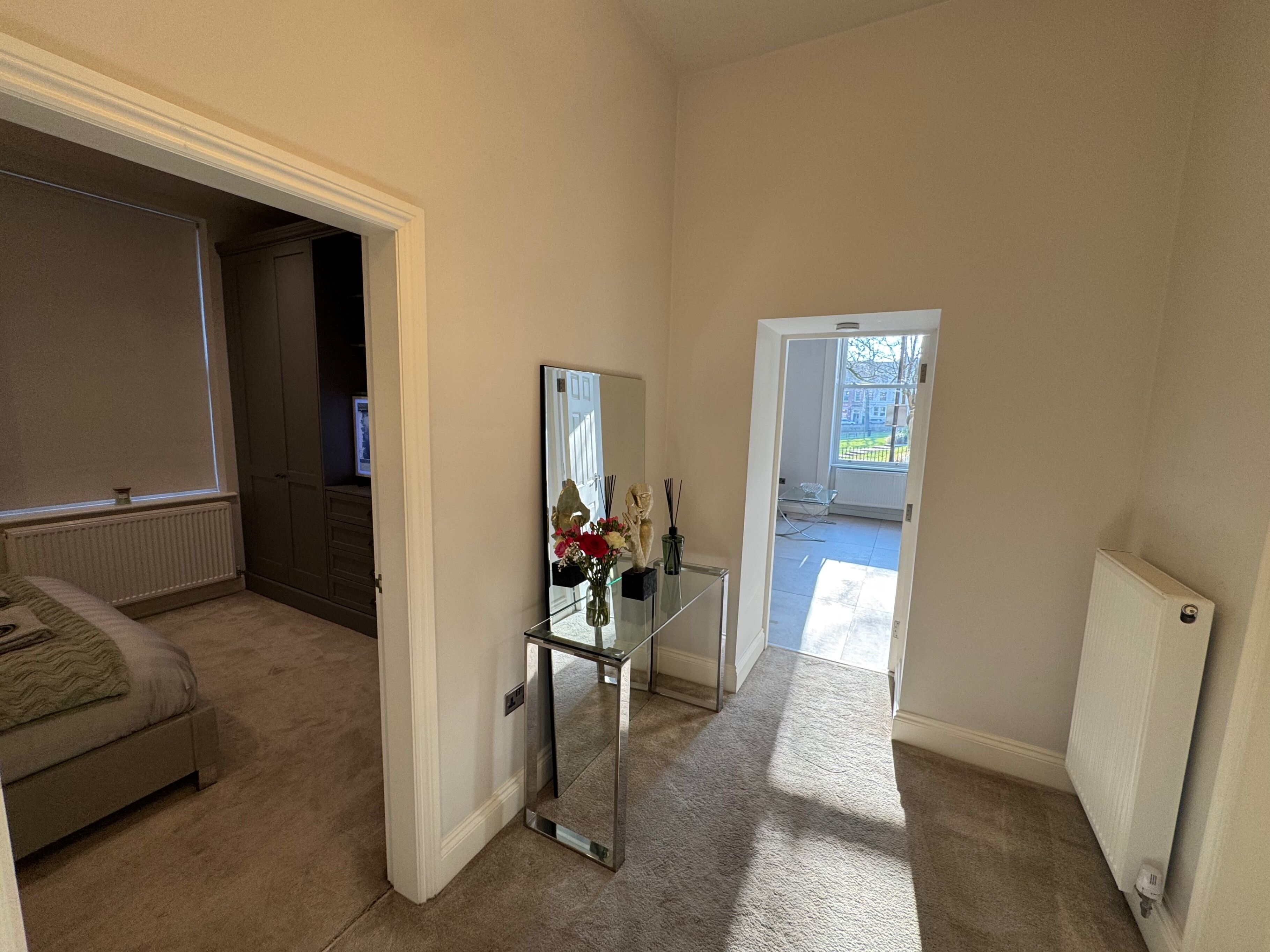 A hallway with a bed, a mirror, and a radiator.