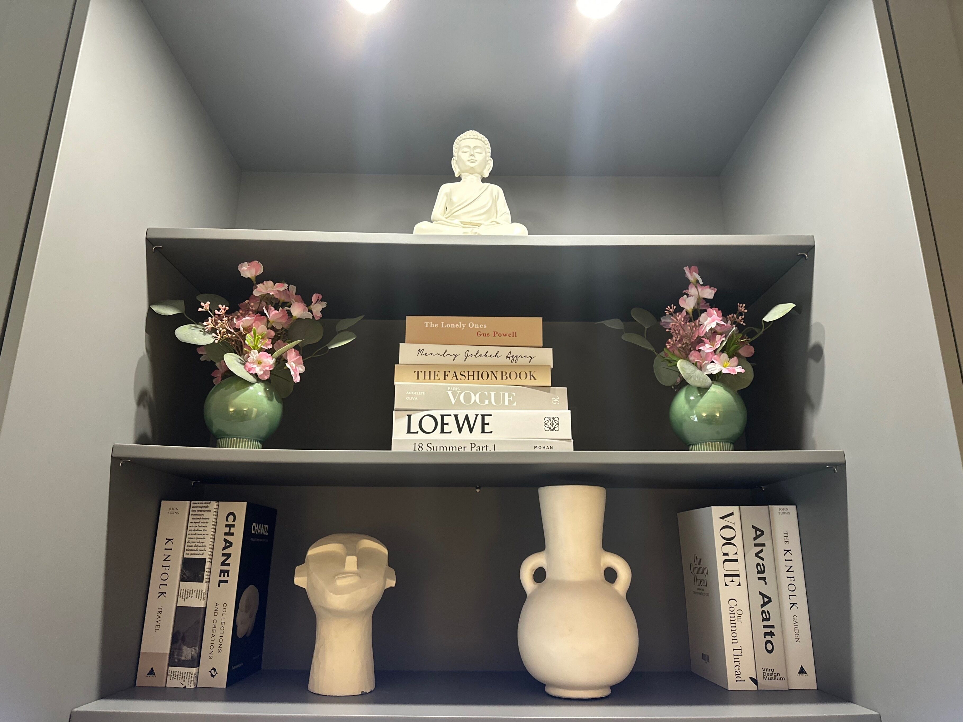 A bookshelf with books, a Buddha statue, and decorative vases.