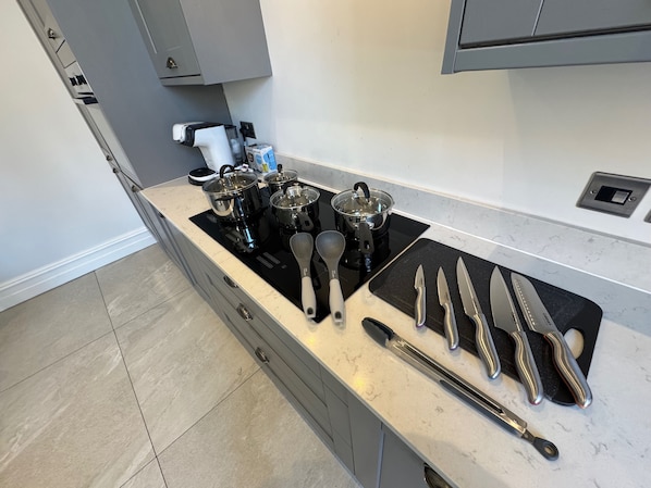 Une cuisine moderne dotée d’une plaque de cuisson à induction noire, de casseroles en acier inoxydable et d’un bloc à couteaux contenant différents types de couteaux.