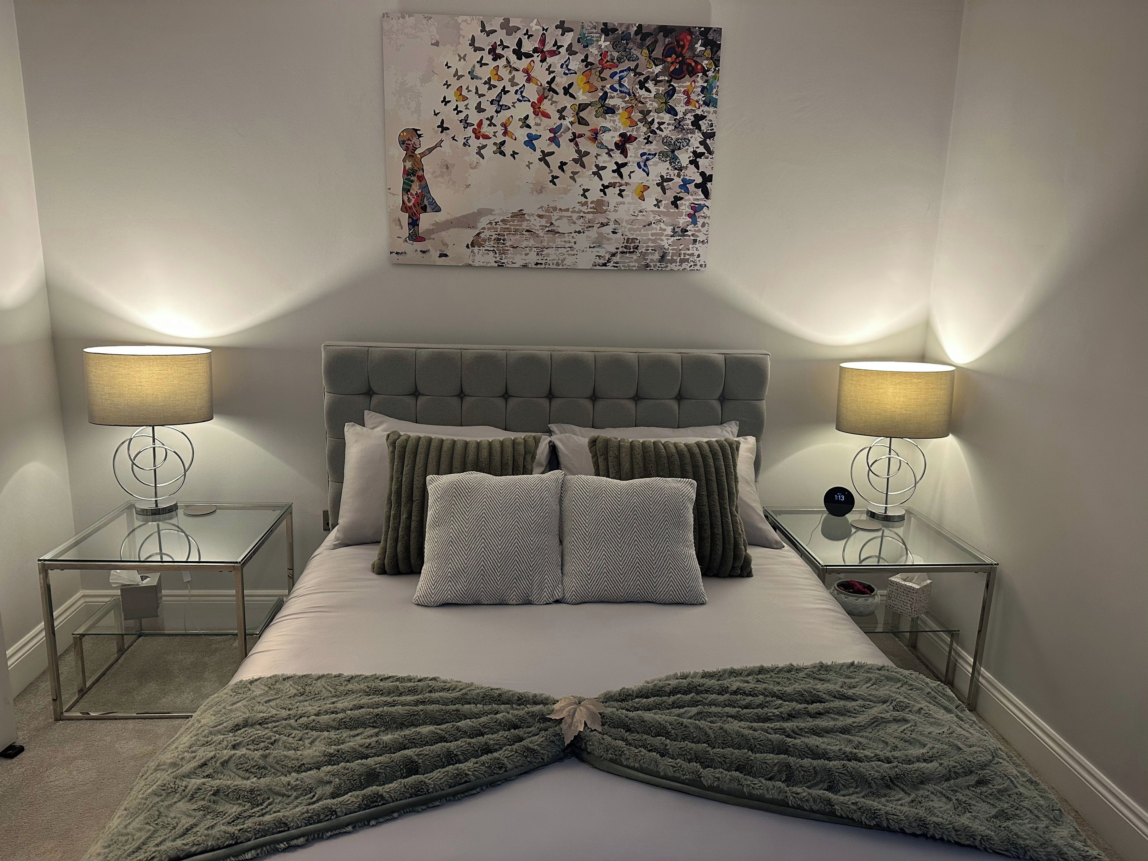 A bedroom with a tufted headboard, a bed with multiple pillows, two bedside tables with lamps, and a wall-mounted artwork.