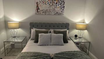 A bedroom with a tufted headboard, a bed with multiple pillows, two bedside tables with lamps, and a wall-mounted artwork.