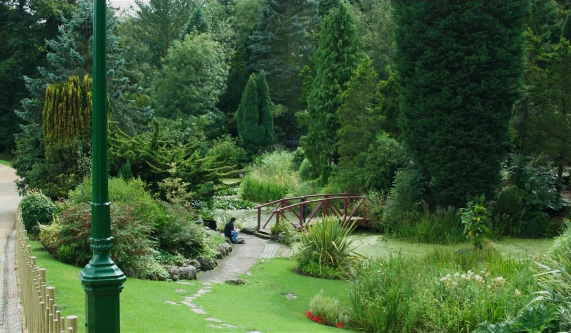 Un jardin luxuriant avec un pont en bois, un sentier et une grande variété de plantes.