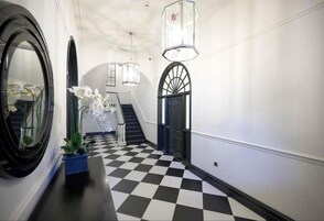 Un pasillo con suelo a cuadros, pared blanco y negro y una puerta azul, además de un espejo.