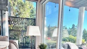 A room with a sofa, a small table with a lamp, and a view through large windows. - Seascape Oasis - 2BDRM - Ocean View - Kitchen (Nanoose Bay)