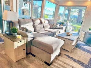Una sala de estar moderna con un conjunto de sofá, una mesita de noche con lámpara y vistas a través de grandes puertas de cristal.